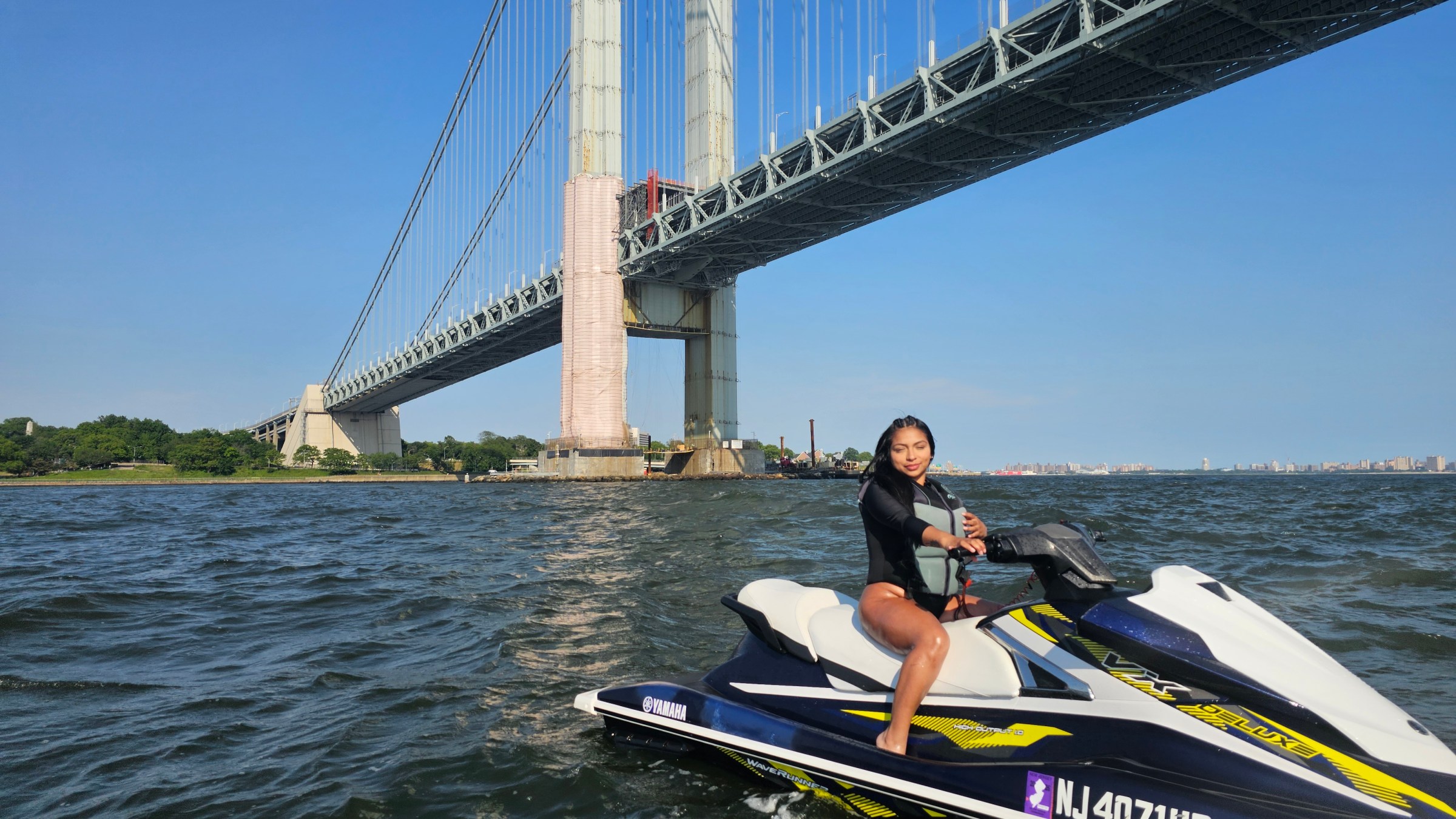 Person on jet ski under large suspension bridge on a sunny day.