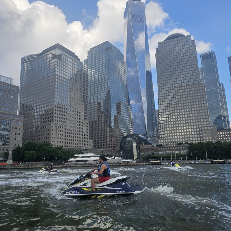 Person jet skiing on a river with city skyscrapers in the background.