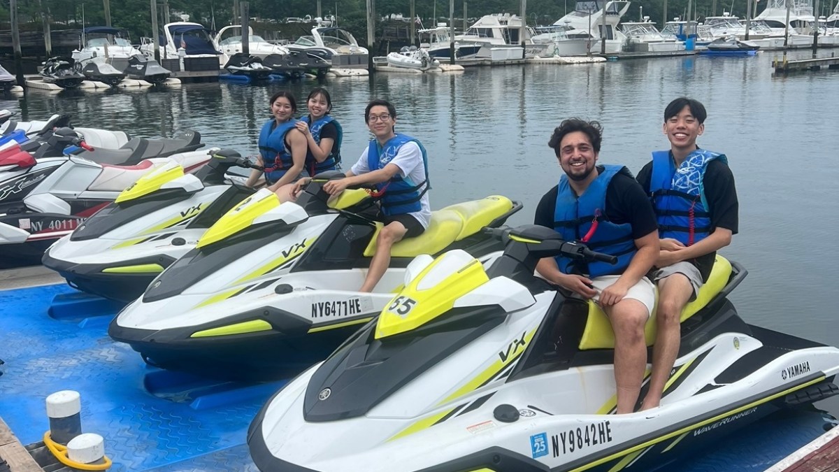 Five people sitting on jet skis at a marina with boats in the background.
