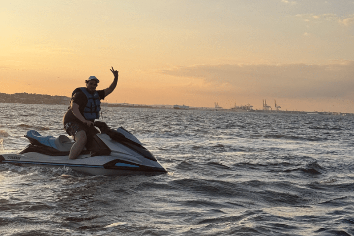 Person on jet ski in ocean at sunset, raising arm in a victory gesture.