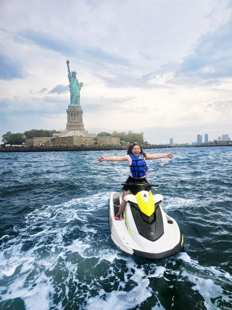 Person on a jet ski near the Statue of Liberty with arms outstretched.