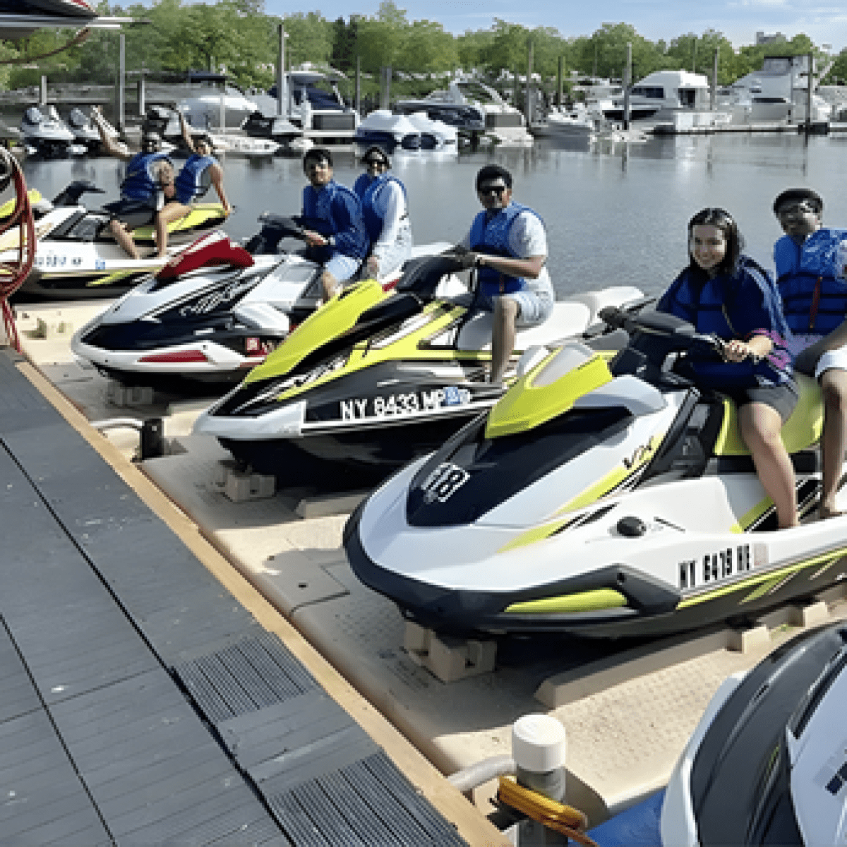 People preparing to ride jet skis at a dock near a marina on a sunny day.