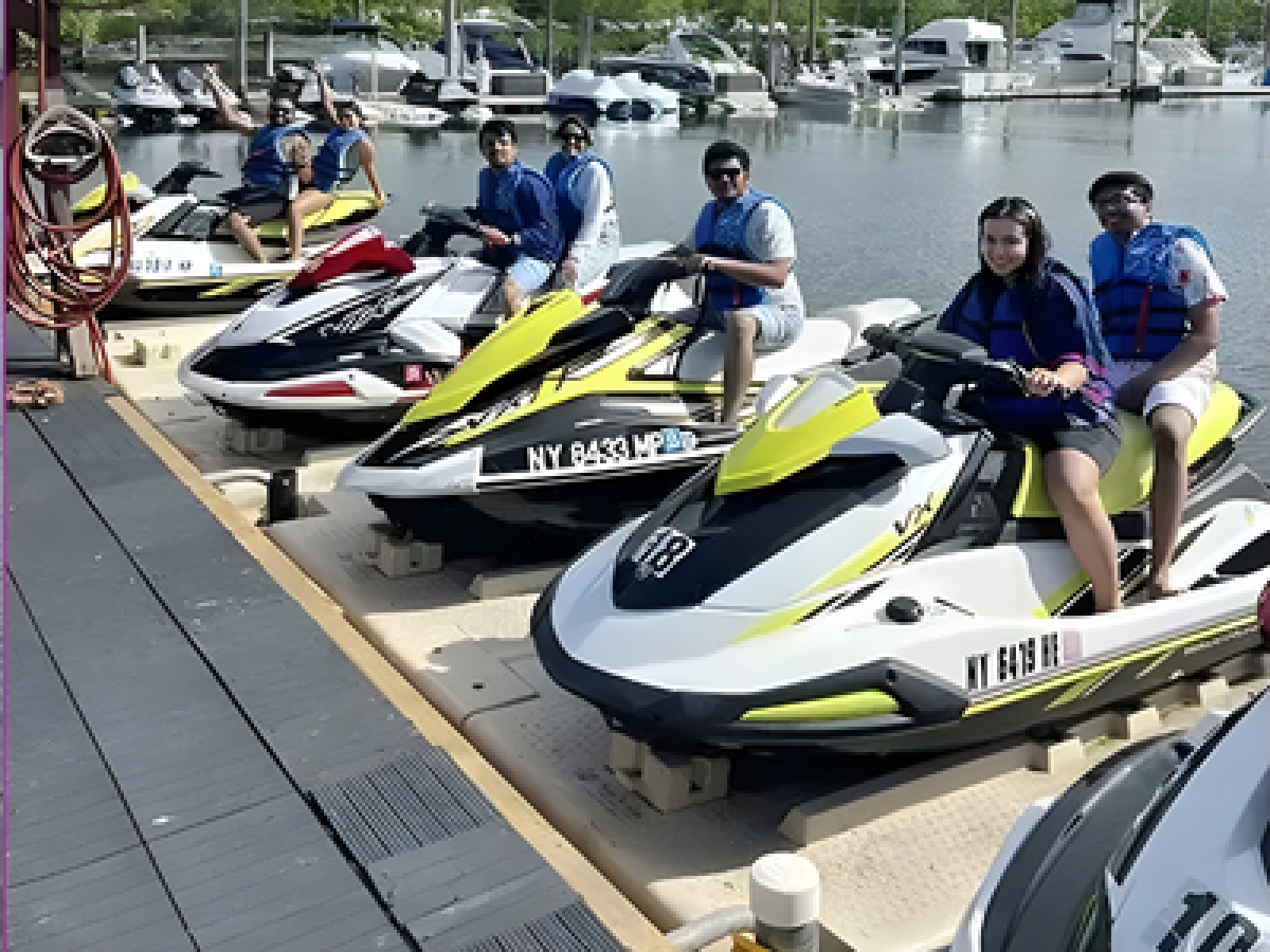 People preparing to ride jet skis at a dock near a marina on a sunny day.