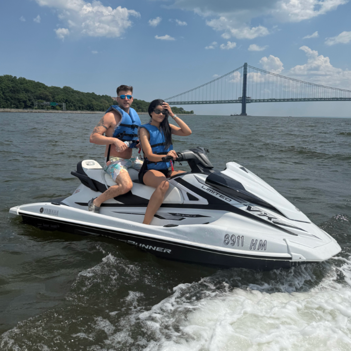 Two people on a jet ski in front of a bridge on a sunny day.
