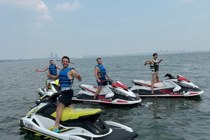 Four people on jet skis on a calm body of water with a city skyline in the background.