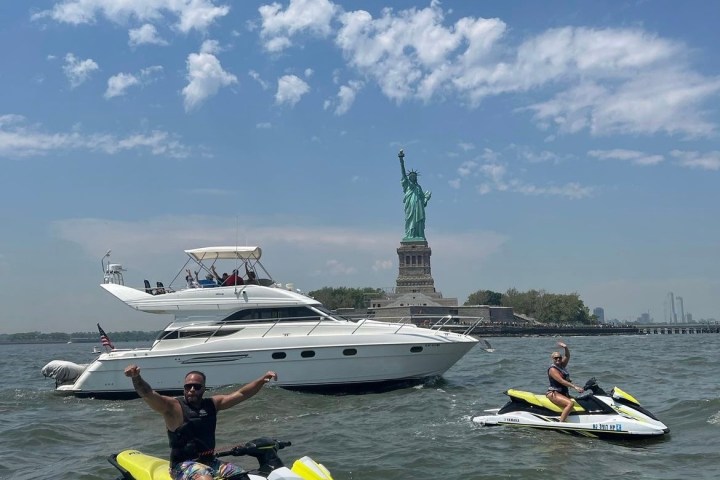 People on jet skis and a yacht near the Statue of Liberty on a sunny day.