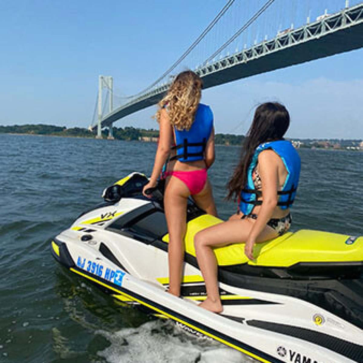 Two people on a jet ski near a large suspension bridge.