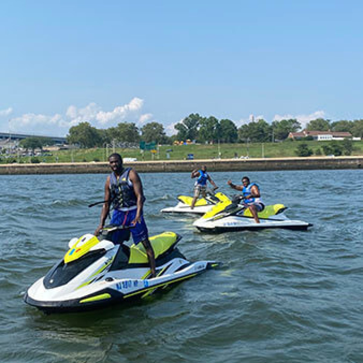 Three people on jet skis in a river on a sunny day.