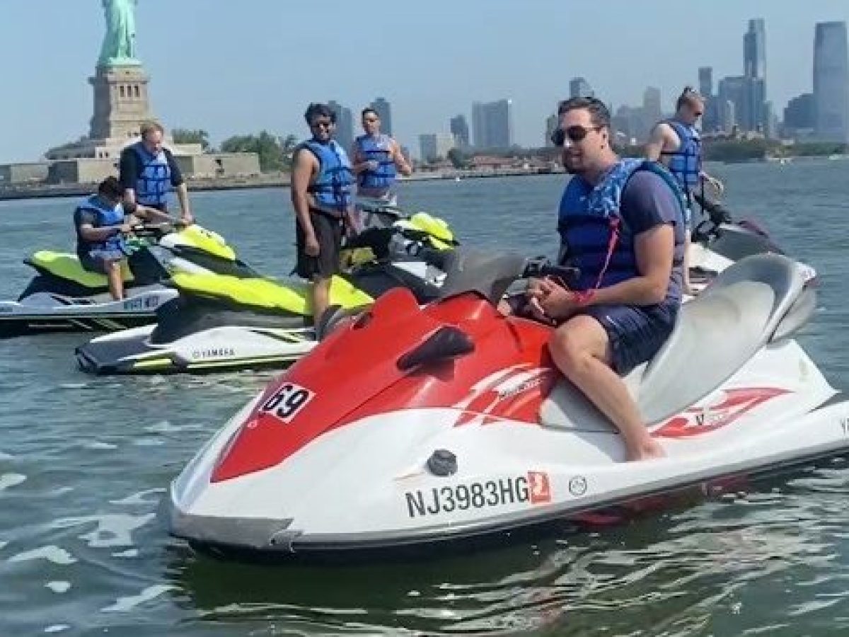 People on jet skis near the Statue of Liberty, NYC skyline in background.