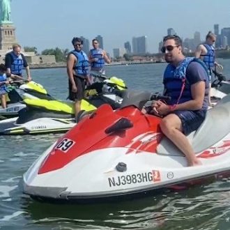 People on jet skis near the Statue of Liberty, NYC skyline in background.