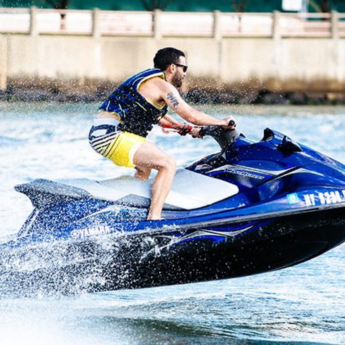 Man riding a jet ski on the water near a concrete wall.