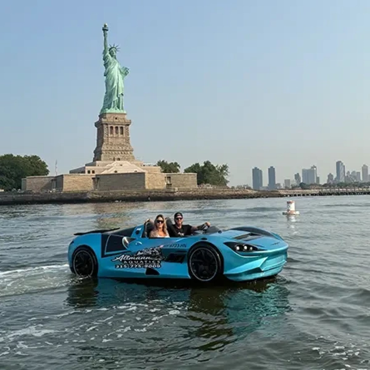 Blue car converted into a boat near Statue of Liberty with city skyline in background.