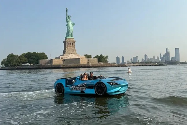 Blue car converted into a boat near Statue of Liberty with city skyline in background.