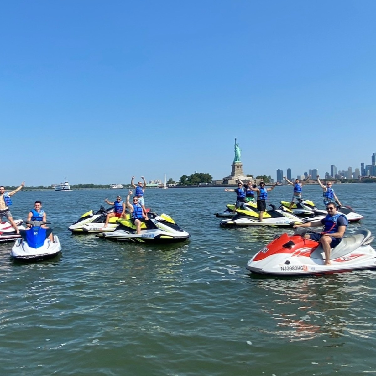 Group on jet skis near Statue of Liberty on a sunny day.