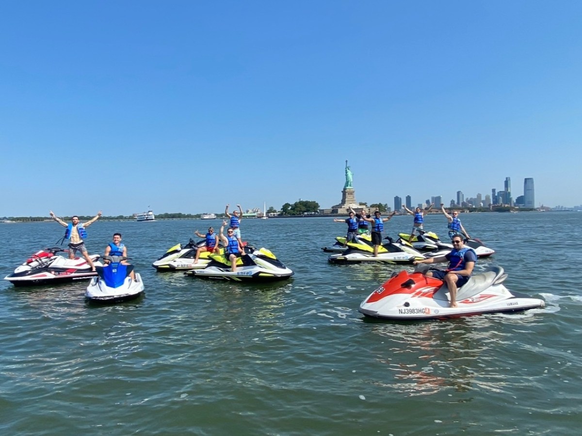Group on jet skis near Statue of Liberty on a sunny day.