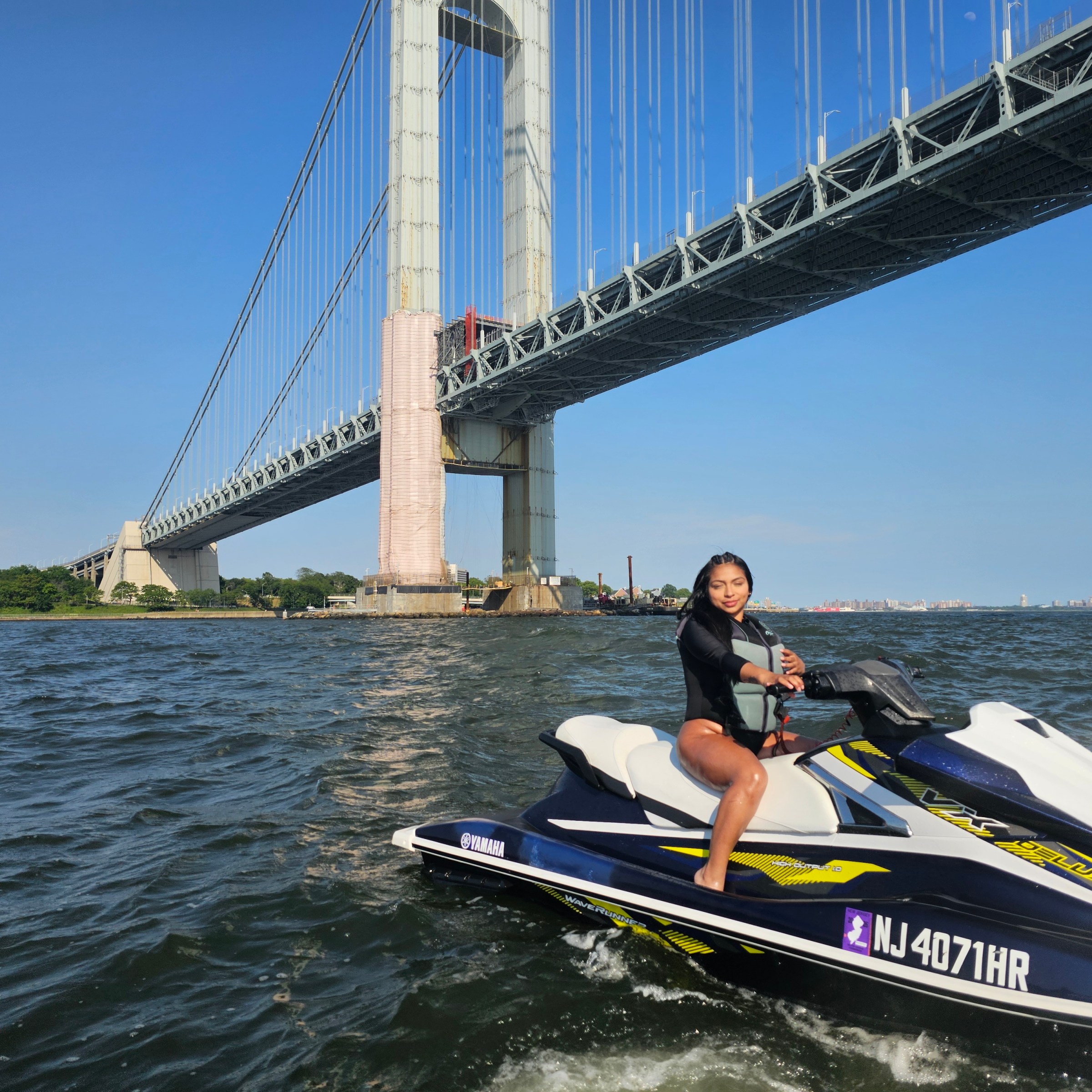 Person on jet ski in water near a large suspension bridge.